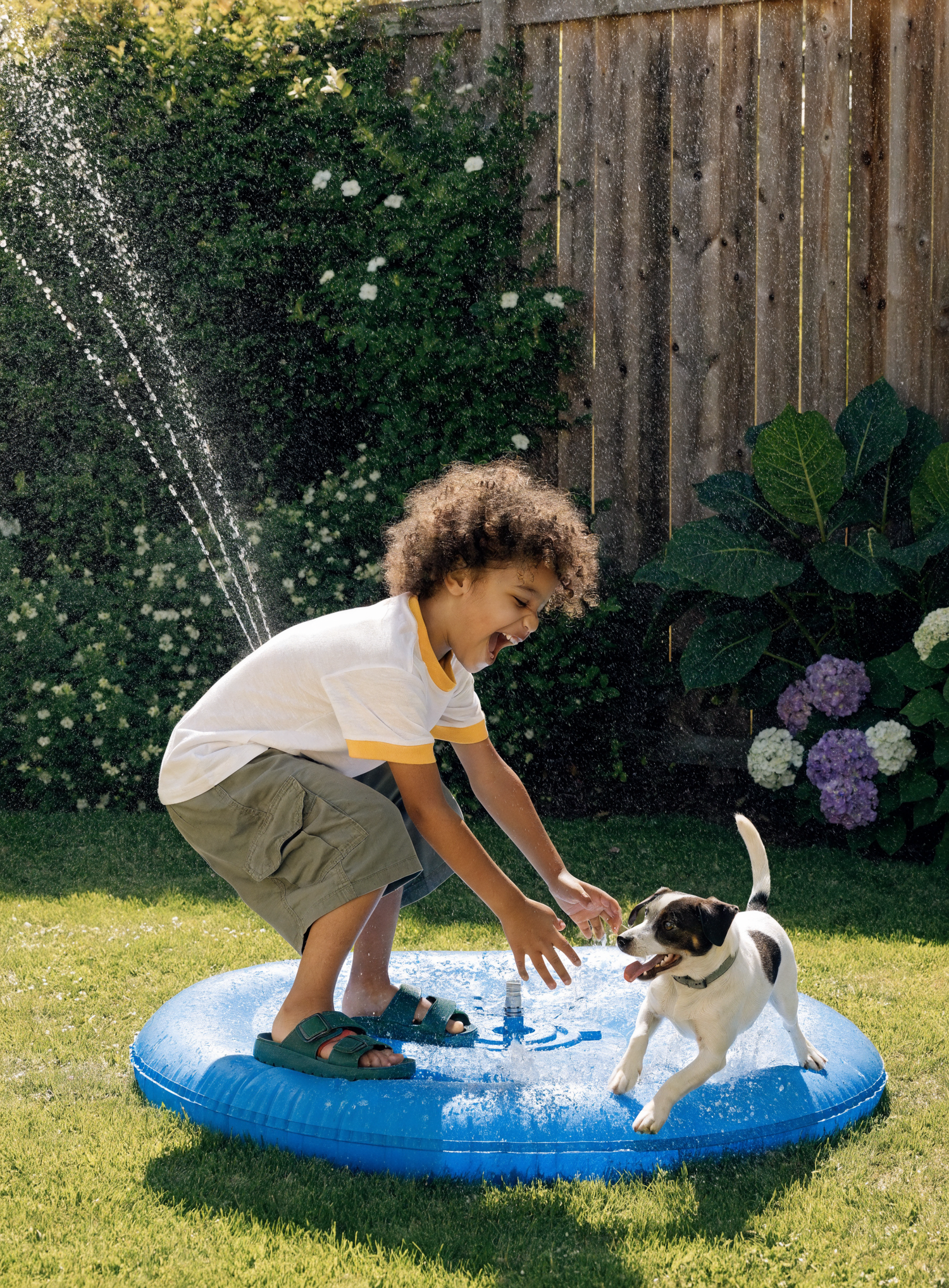 Enfant et chien jouant sur le tapis d'eau à jet AquaSplash dans un jardin ensoleillé